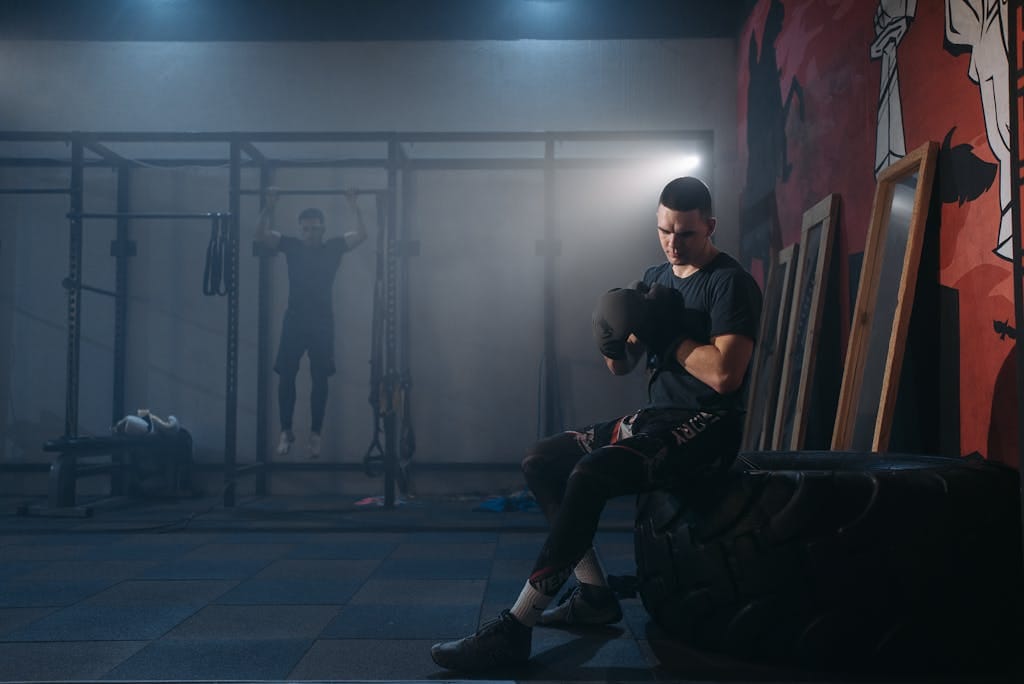 A focused boxer sitting on a tire, preparing for a workout in a well-equipped gym.